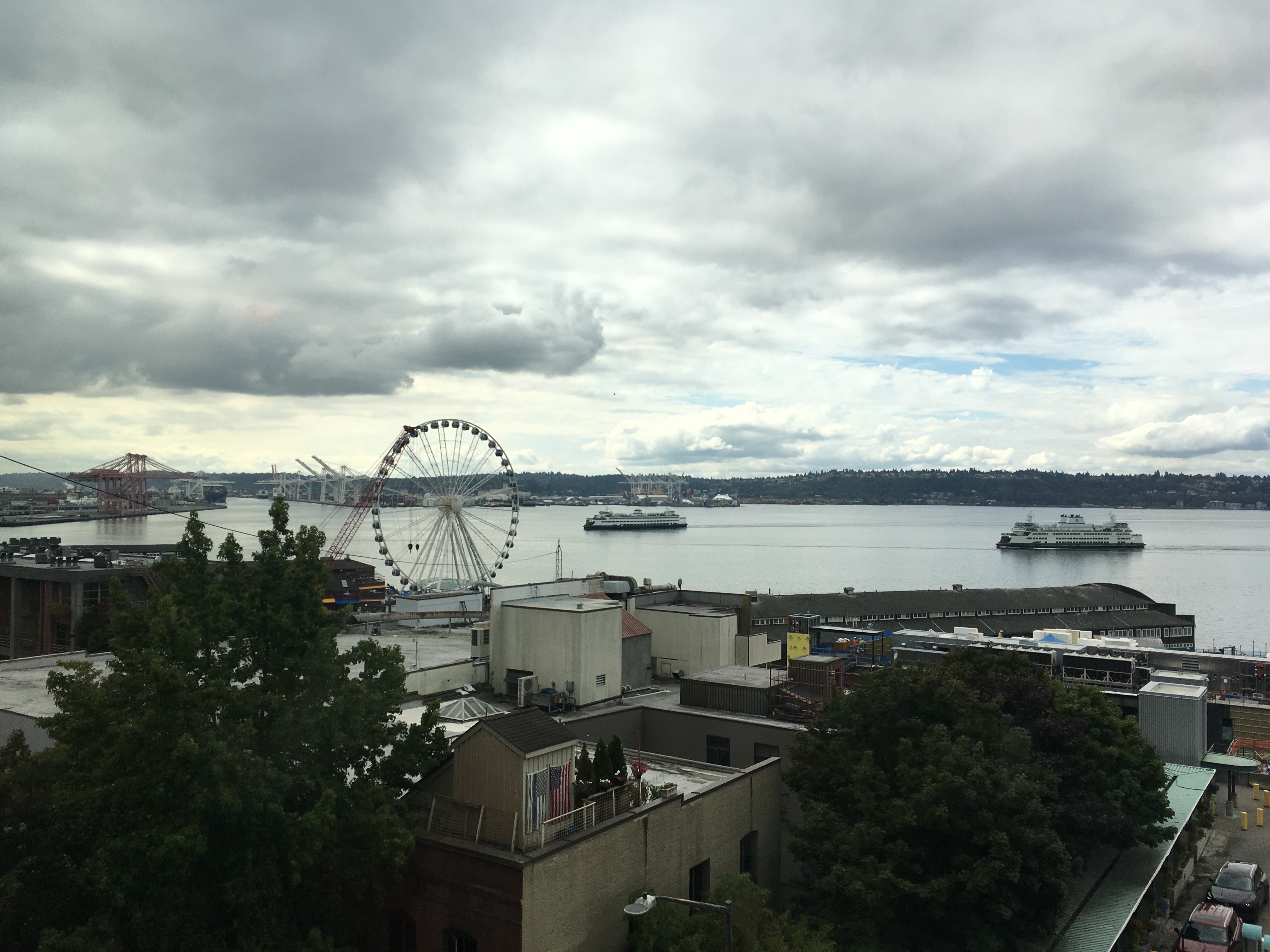 Cloudy, grey day looking out over Seattle harbour, with ferris wheel on the pier and two ferries approaching the dock