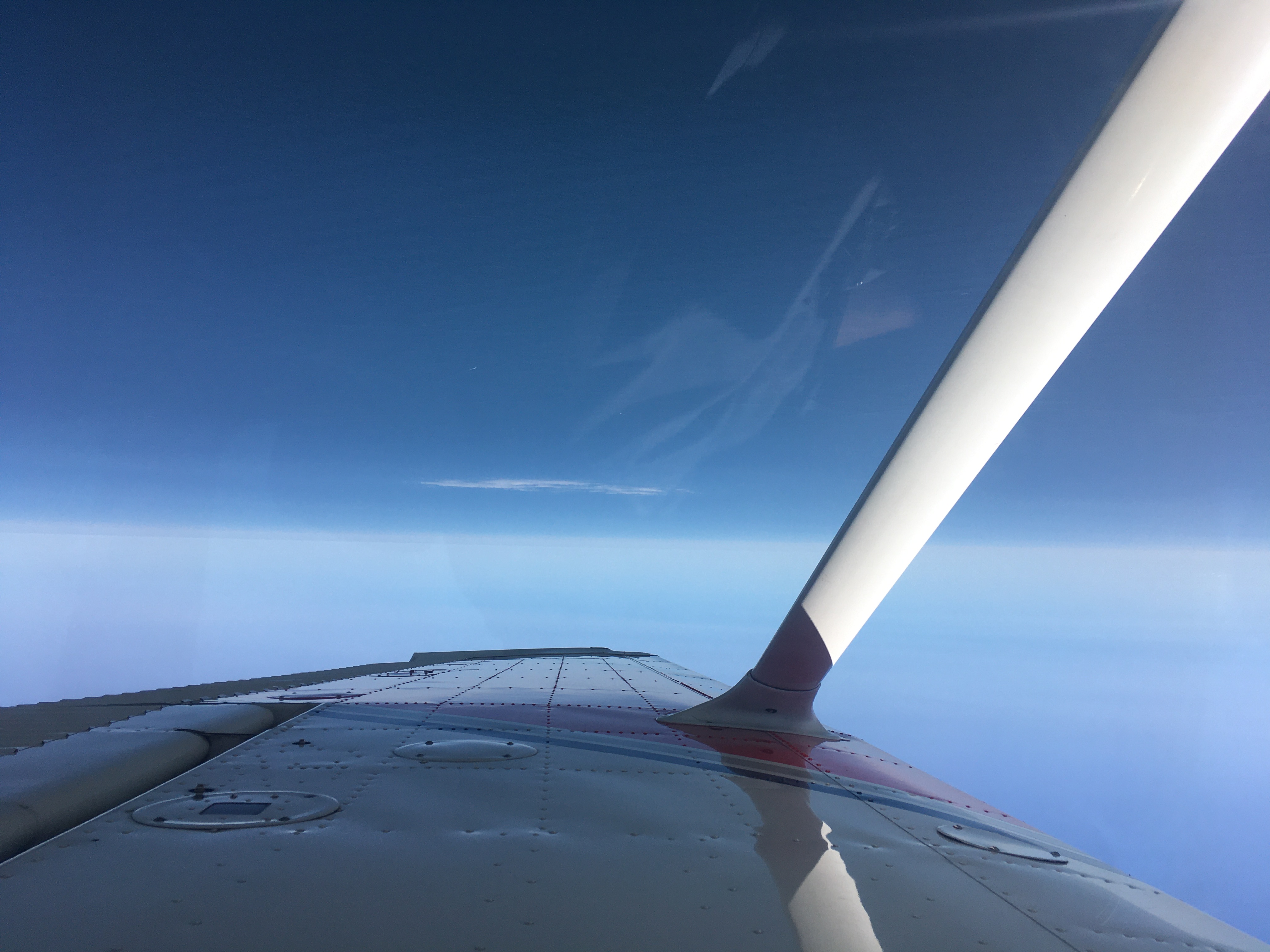 Under the wing of the airplane, the pacific ocean stretches to the horizon, marked by only one small bank of white cloud