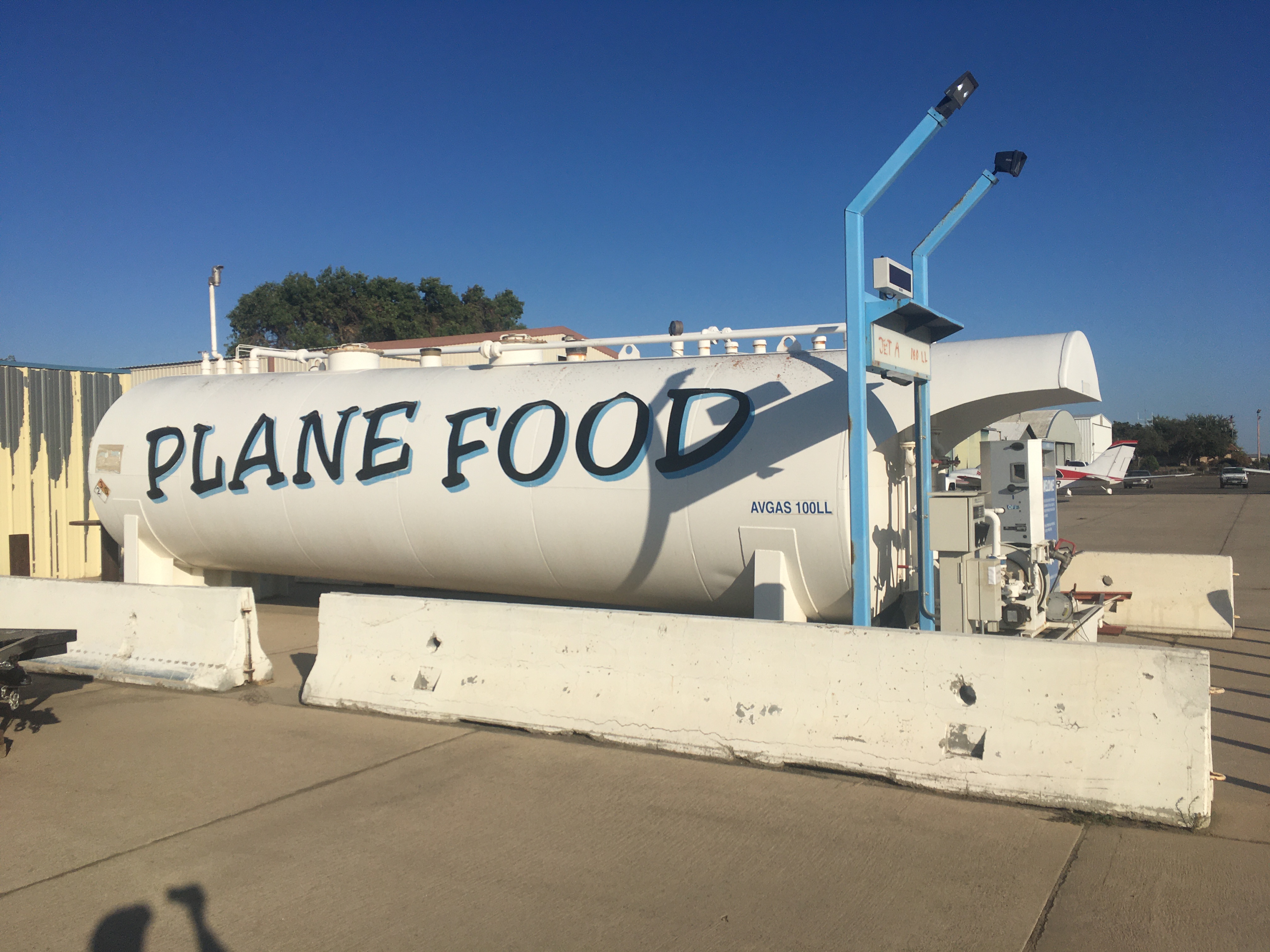 A large white tank for aviation fuel has a label in metre-high letters that says 'PLANE FOOD'