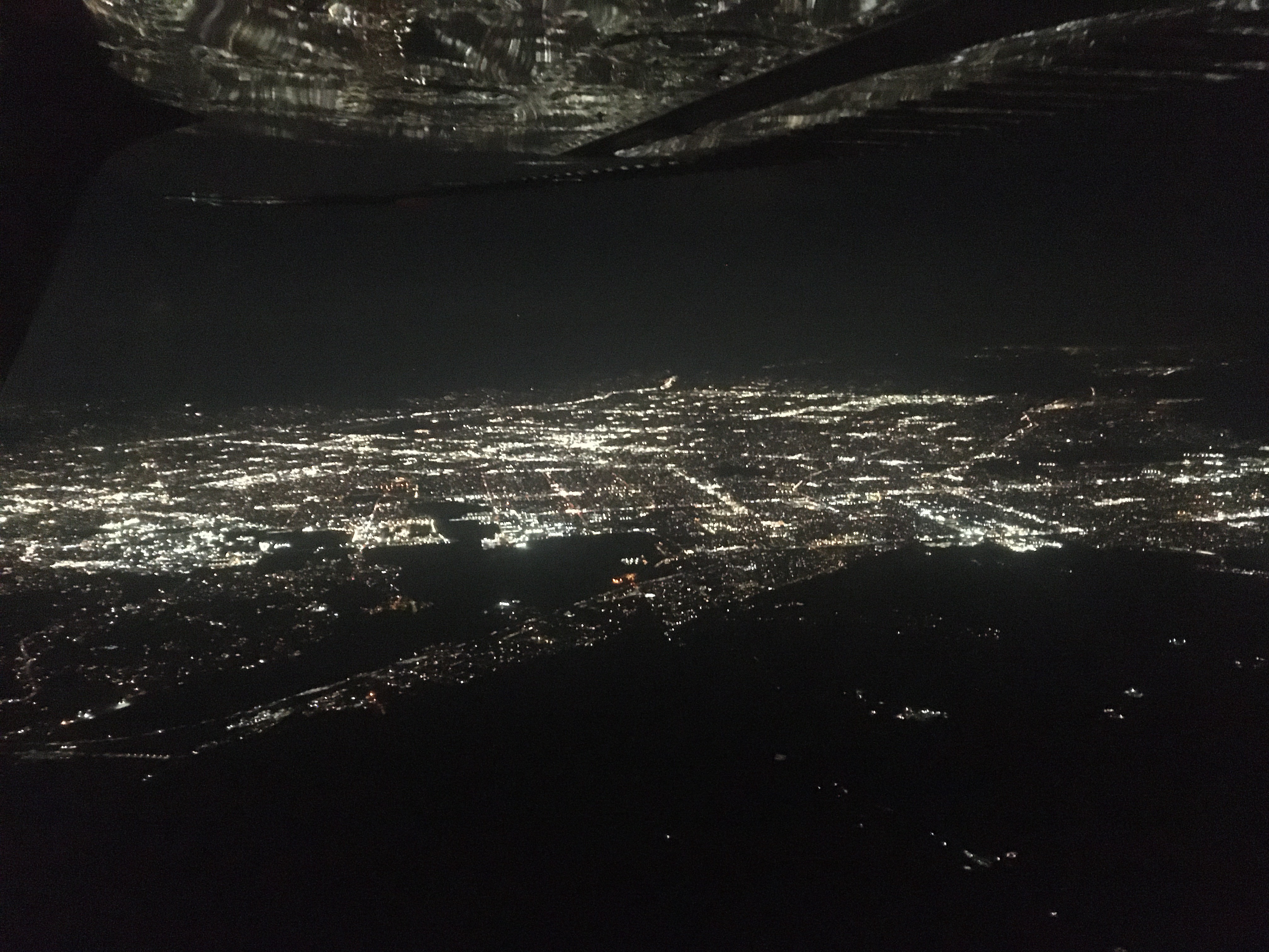 Aerial view of city lights at night, reflecting in the wing of the airplane
